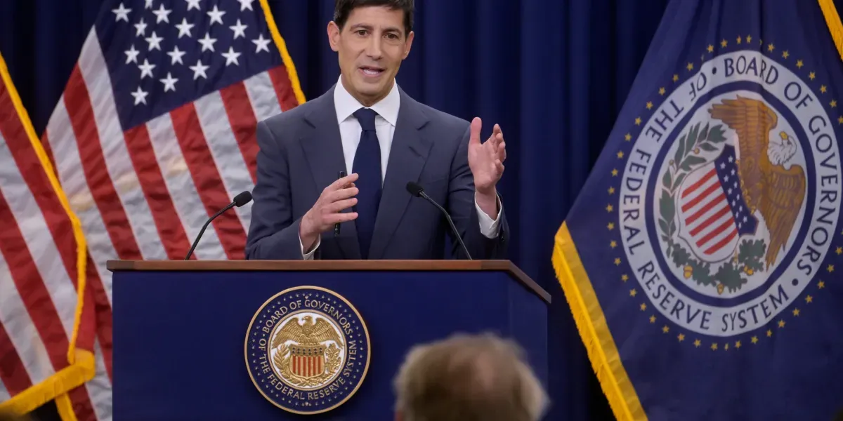 A Federal Reserve official speaking at a press conference podium bearing the Board of Governors seal