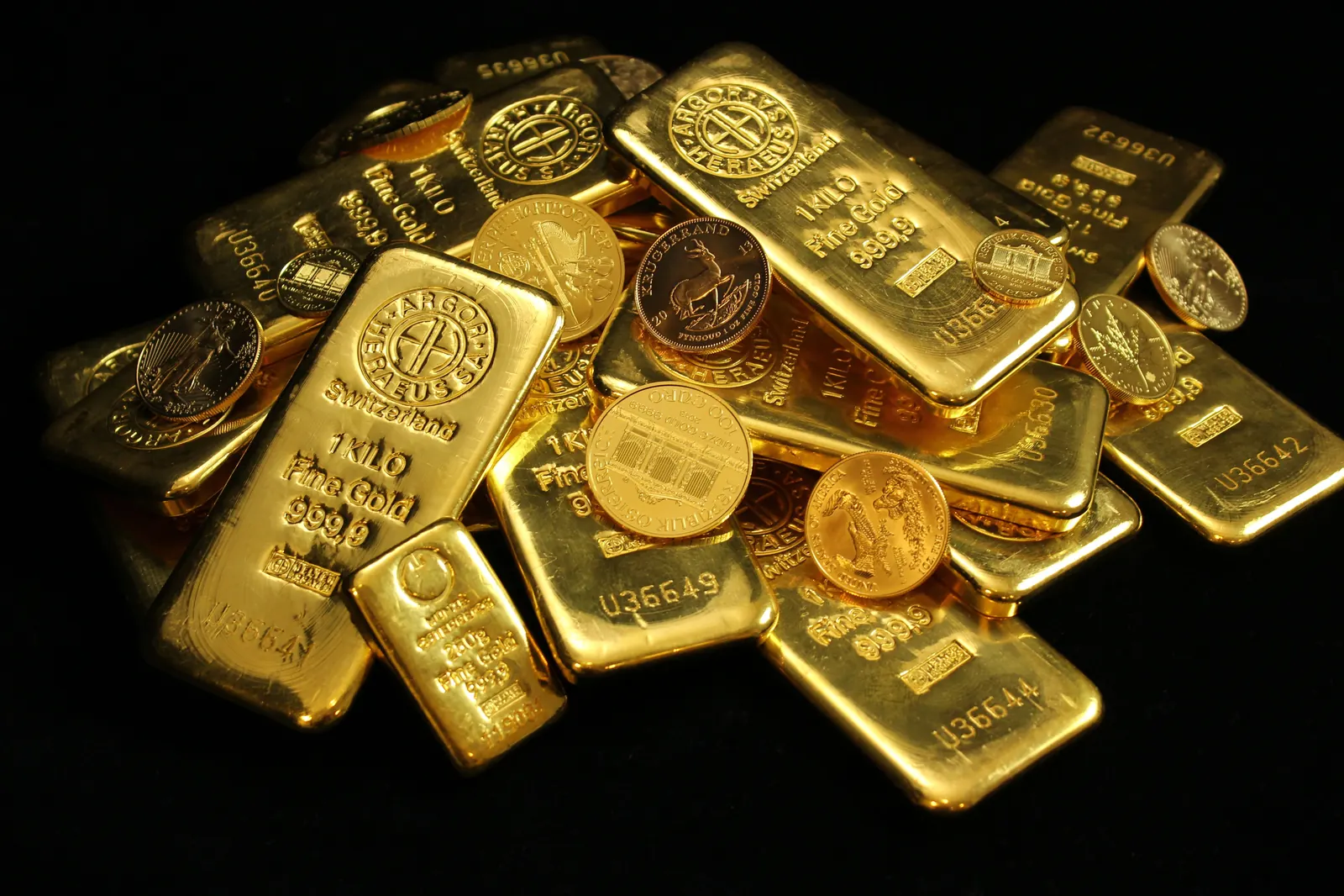 A pile of gold bars and gold and silver coins on a dark background